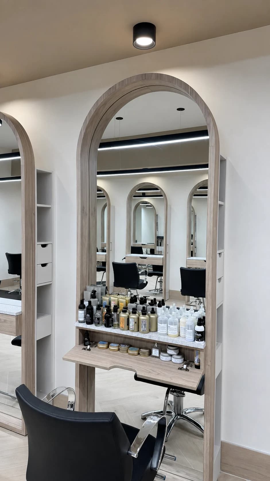 Individual styling station with an arched mirror, black chair, and hair products