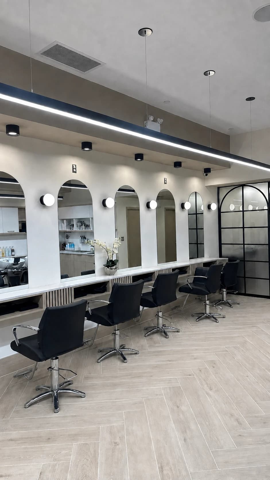 Salon styling stations with black chairs, arched mirrors, and globe wall lights