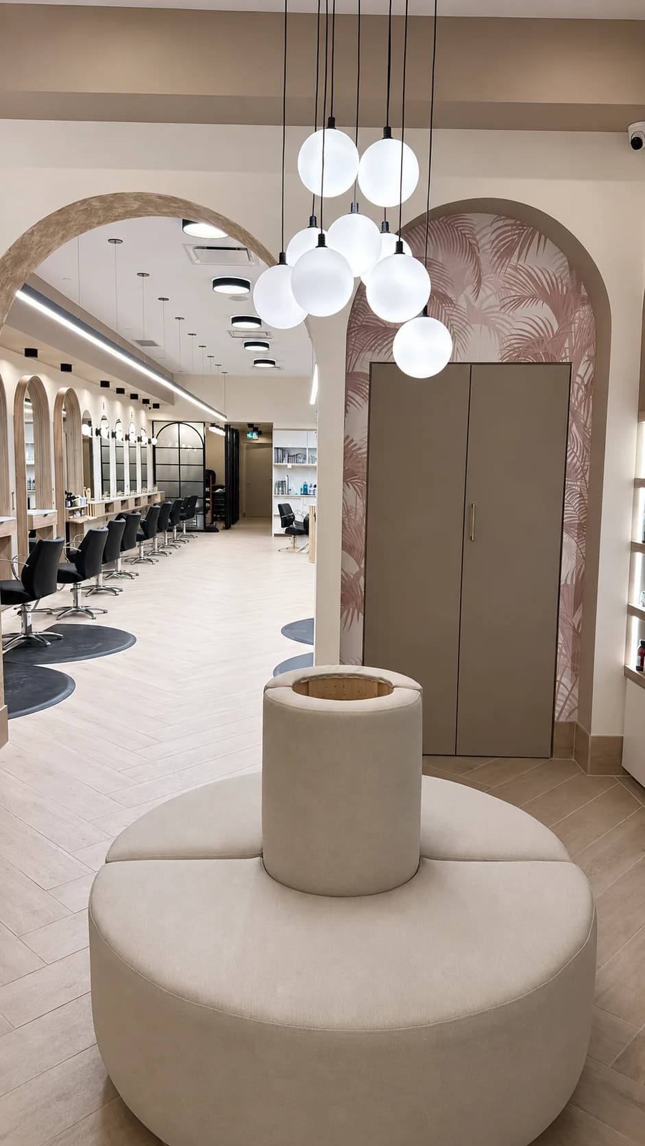 Curved reception bench beneath globe lights beside the archway to the styling floor