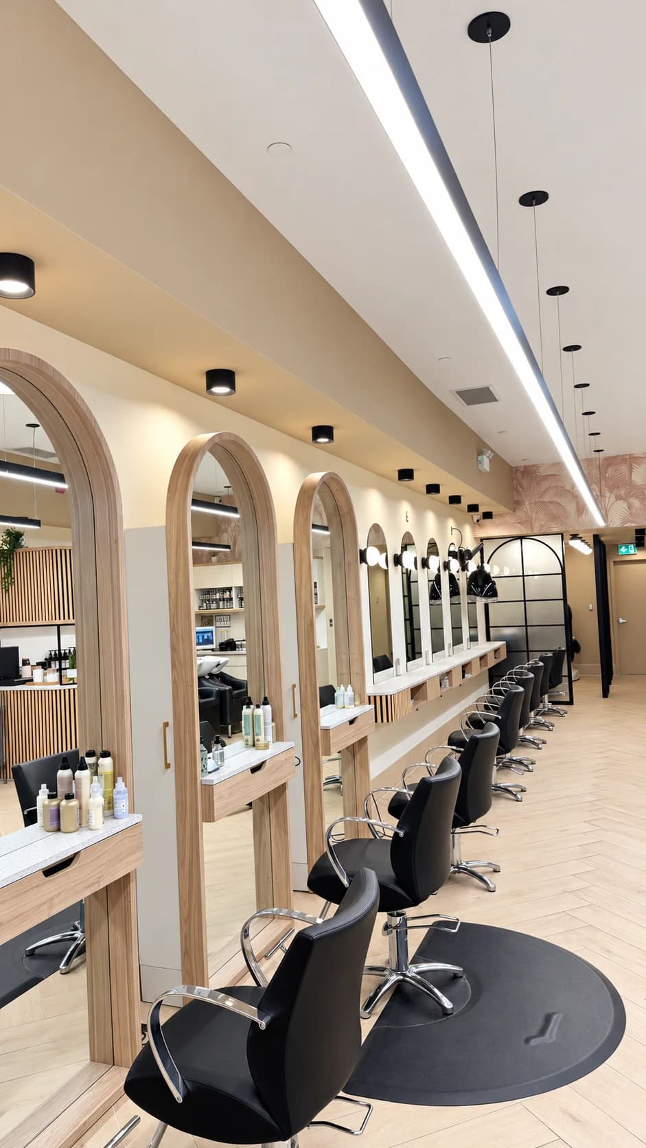 Salon styling floor with wood-framed arched mirrors, black chairs, and pale wood flooring